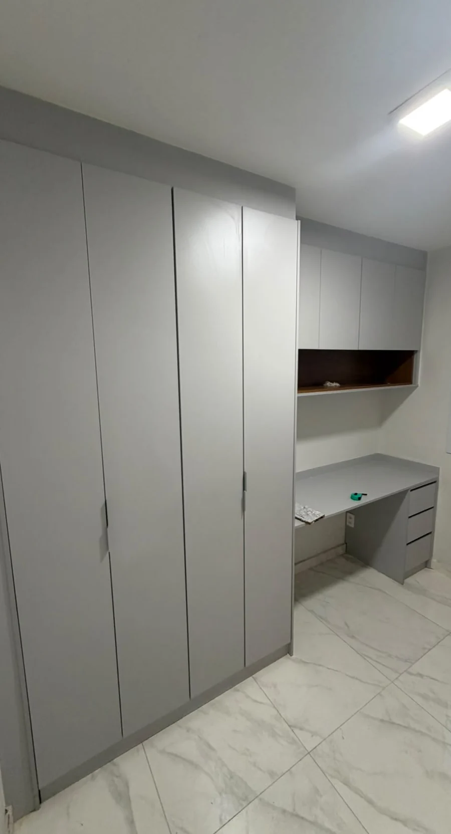 Quarto com guarda-roupa de portas cinzas e escrivaninha integrada sob nicho de madeira.